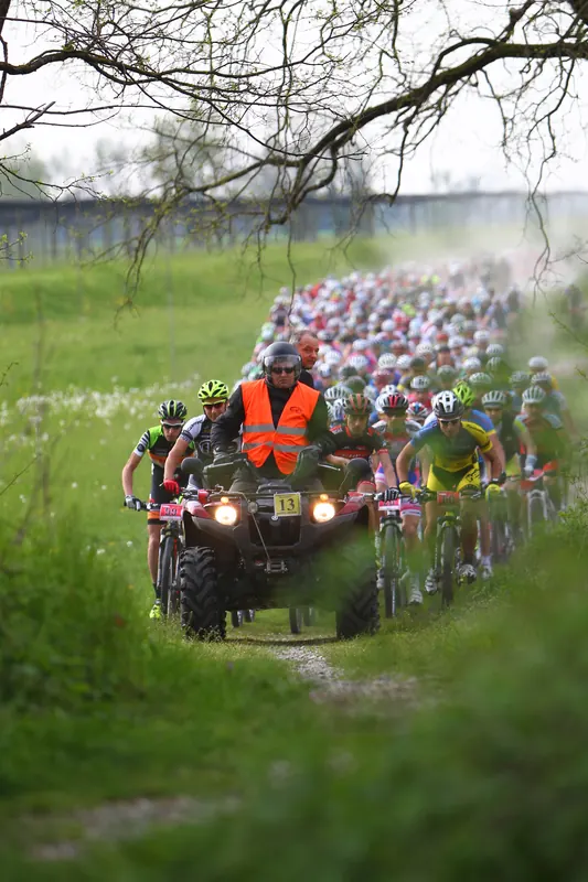 Gruppo di ciclisti in gara su una strada di campagna seguito da una moto